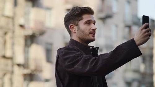 Smiling man video chatting using phone in city