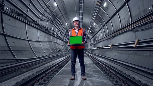 Full Body Of Asian Male Engineer Smiling And Showing Green Screen Laptop In Subway Tunnel