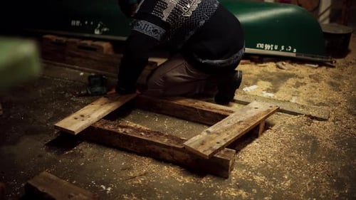 A Man is Using a Drill to Insert Nails and Secure the Wooden Plank - Static Shot