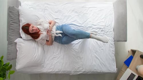 Young Woman Uses a Mobile Phone to Browse Internet on Bed in Room Top View