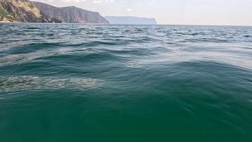 Sea Water Surface Camera Flies Over the Calm Azure Sea with Volcanic Rocky Shores on Background