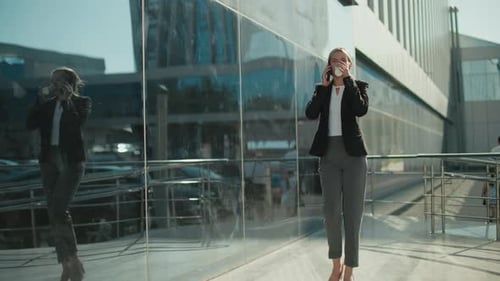 Professional Lady Walking with Coffee on Phone Call Near Glass Building Exterior