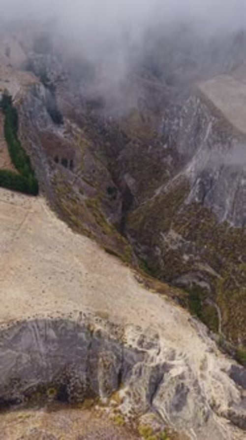 Vertical Format Video of Misty Clouds Hovering Above Deeply Carved Mountain Valley Within Rugged