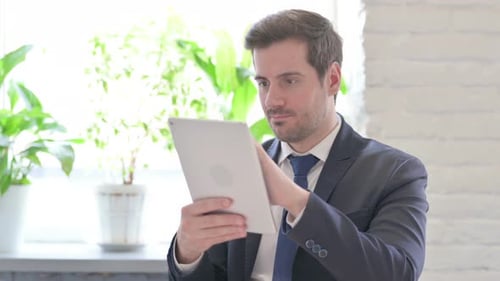 Young Businessman Celebrating Success on Tablet in Office