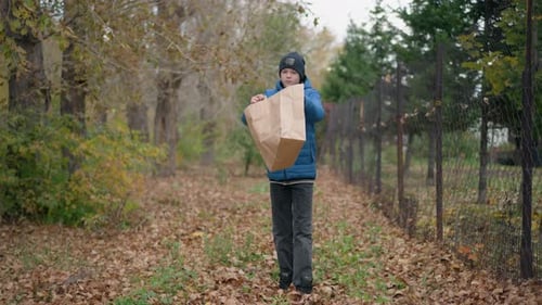 Boy Drops Leaves From Paper Bag in Autumn