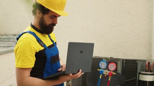 Man Repairing Air Conditioning Unit With Laptop