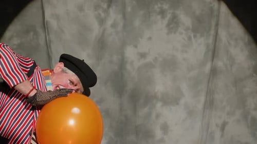 Clown with balloon juggling against grey background