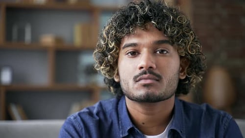 Portrait of serious young handsome man sitting on sofa in living room at home. Head shot