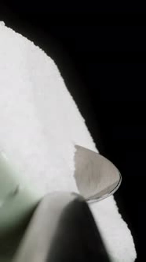 Vertical video. I Sprinkle Sugar into A Glass with A Spoon, First-Person Macro View. On A Black
