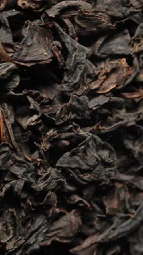 Vertical video. Dry black tea leaves, macro background, rotating in a jar.