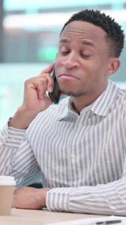 African Businessman with Coffee Talking on Smartphone in Office, vertical video