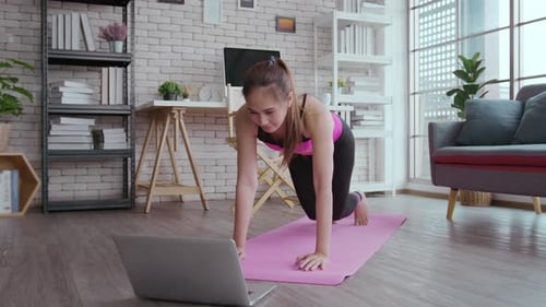 Fit young woman practicing yoga at home via online class with professional instructor