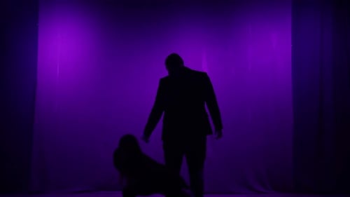 Zwei silhouettierte Figuren auf der Bühne, die einen Tanz und ein Lied in lila Licht aufführen