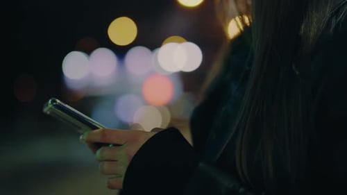 Young Woman Texts Message on Smartphone Standing on City Street Late in Evening