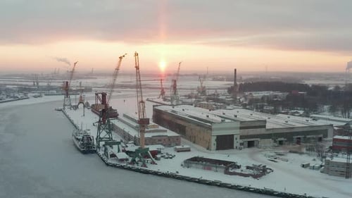 Luftbild des Industriehafens im Winter, bedeckt mit Schnee und gefrorenem Wasser. Wunderschönes goldenes Sonnenlicht