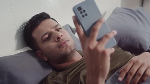 Young Adult Lying in Bed Using Smartphone