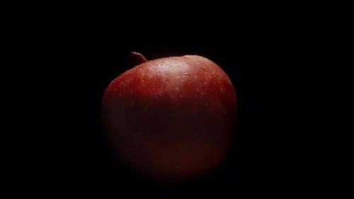 A red apple in water droplets, rotating on a black background, close-up. The apple appears from the