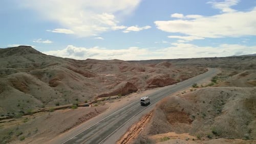 Tracking shot panning around an RV that drives along a quiet road in the desert.