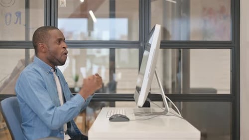 Excited African Businessman Celebrating Success on Desktop in Office