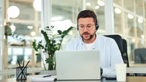 Focused Businessman in Headset Works on Laptop in Modern Office