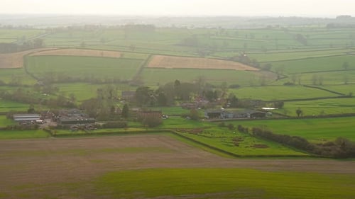 Expansive Rural Farmland Landscape with Distant Farm Buildings Among Green Fields Agricultural