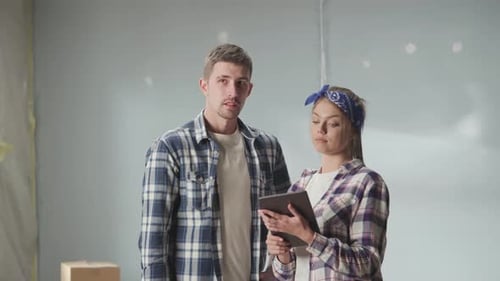 Feliz pareja joven con camisas a cuadros usando una tableta para planificar las renovaciones en su apartamento