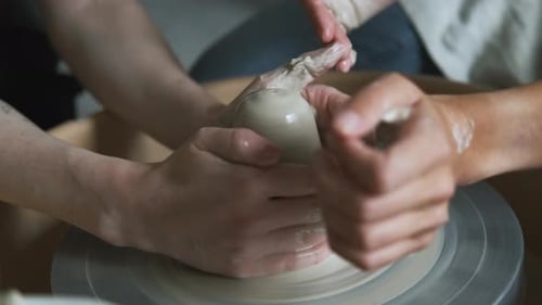 gros plan des mains du maître et de l'apprenti sur un tour de potier