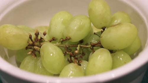 Fresh green grapes, ready to be eaten, are seen in a white bowl.