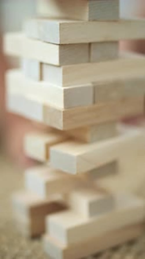 Child's Hand Pulling Out a Brick From a Wooden Tower Playing Jenga