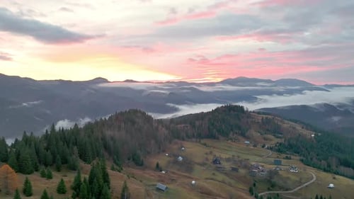 Aerial Panoramic View of Mountain Village with Scattered Houses on Green Hills During Pink Sunset