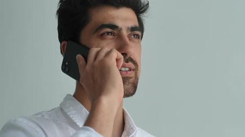 Gros plan du visage d'un jeune homme barbu positif parlant au téléphone portable ayant une conversation sur un smartphone