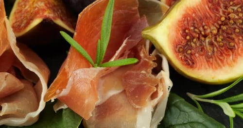 Figues, jamon et feuilles d'épinards sur une planche de service en pierre noire. Set de snacks.
