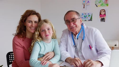 Portrait of Doctor and Little Girl with Her Mother Smiling at Camera at Clinic