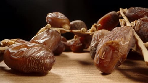 Dried dates on a branch lie on a wooden table and smoothly emerge into the light.