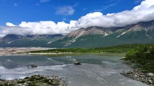 Rising over the river reflecting the beautiful mountains covered with fluffy clouds at the tops.