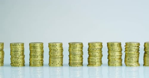 A businessman in a suit and tie has before him many stacks of gold coins. The businessman counts a