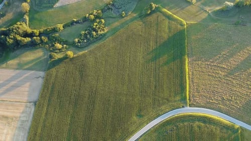 Drone rises from a lush green field, unveiling vast landscapes with patches of ready-to-sow brown la