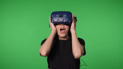 Portrait of a Young Woman Wearing Virtual Reality Glasses on a Green Background