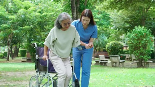 Woman Assists Senior Getting Up from Wheelchair Outdoors