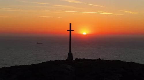 Silhouette of Cross at Sunrise Over Ocean Horizon