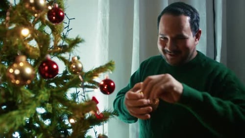 Man Decorating Christmas Tree with Ornaments at Home