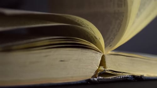 Slow motion, close up of an old, vintage, open book with pages turning on the wind, on a dark room w