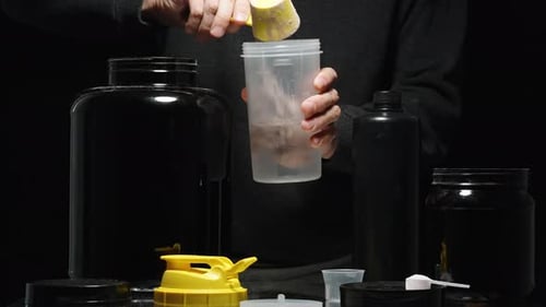 Chocolate Protein Powder Is Poured Into A Shaker With Water. Black Cans With Numerous Supplements On