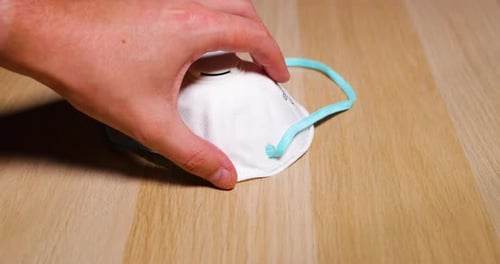 Men's hands putting white protective mask FFP2 on face and nose from wooden table on which lies prot