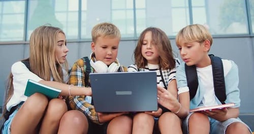 Back to school. Group of teenage school children using laptop sitting on stairs outside high school