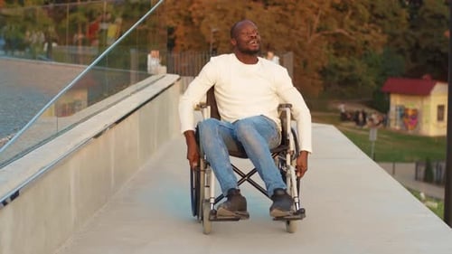 Happy Handsome Disabled Man Rides in Wheelchair at Sunlight Smiling Sing in Park Paralysis