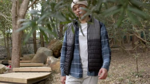 Young man in forest wearing beanie and vest, looking up at trees