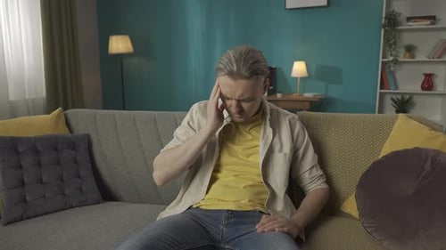 Medium Video of a Middleaged Man Sitting on a Couch Sofa Massaging His Temples and Head Due to a