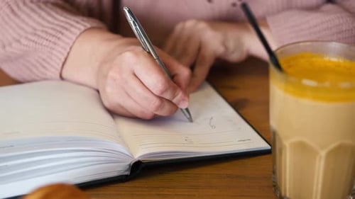 Woman's Hand Writing 2024 New Year Routine Resolutions on Desk Cafe Restaurant Interior Background