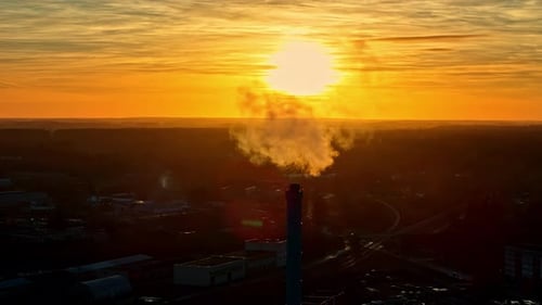 Landscape of smog haze fumes coming from city industrial tower with orange sun setting in horizon ba